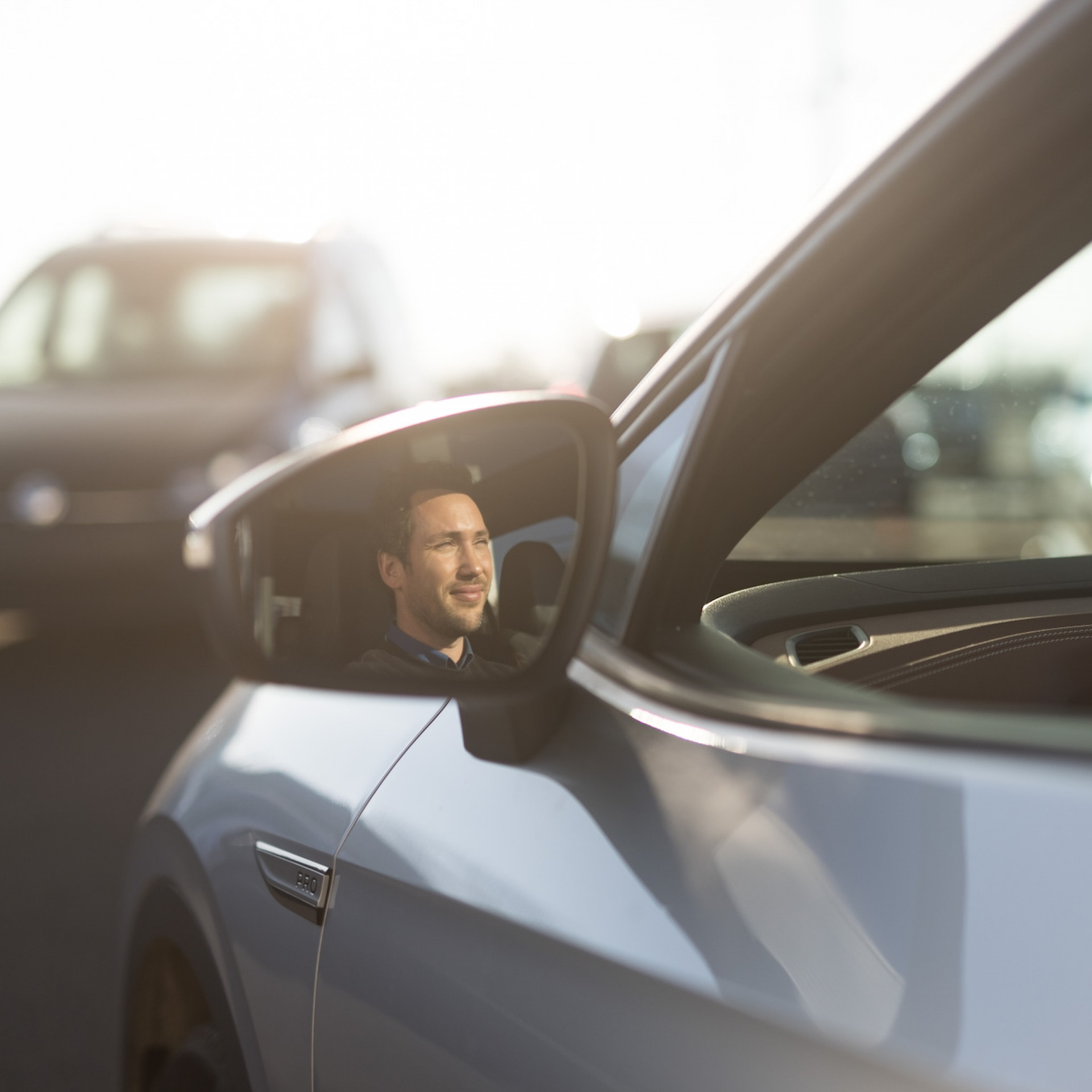 Eine Privatperson sitzt im Fahrersitz ihres Elektroautos und schaut in den Seitenspiegel.